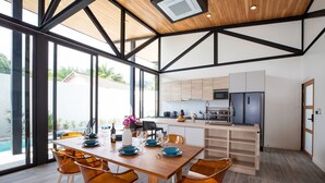 A modern kitchen with a wooden table and chairs, a built-in oven, and a view of the outdoors. - New 19m Eco Pool Villa Sunset Garden 10 (Rawai)