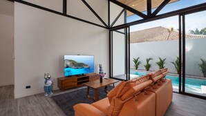 A modern living room with a large TV, a sofa, and a view of a swimming pool. - New 19m Eco Pool Villa Sunset Garden 10 (Rawai)