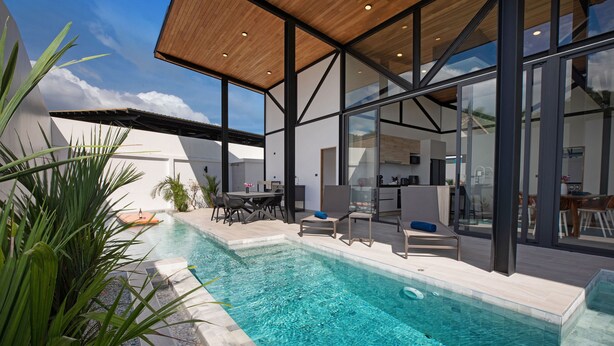 A modern outdoor pool area with a clear blue pool, surrounded by glass walls and wooden ceiling. - New 19m Eco Pool Villa Sunset Garden 10 (Rawai)