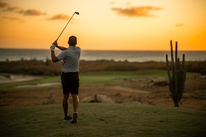 Una persona jugando golf en un campo con un atardecer de fondo.