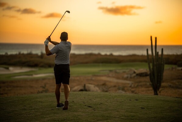 A person playing golf on a course with a sunset in the background.