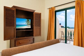 Ein Hotelzimmer mit Fernseher, der eine Strandansicht zeigt, einem Balkon mit einem Stuhl und Vorhängen.
