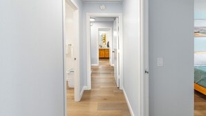 Ein schmaler Korridor mit Holzdielen, weißen Wänden und einer Tür zu einem Schlafzimmer mit einem Bett.