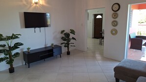 A living room with a TV mounted on the wall, a black entertainment unit, a potted plant, and a sofa. - Beautiful modern retreat with stunning views of mountain ranges & Seaview (Plymouth)