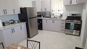 A modern kitchen with stainless steel appliances, white cabinets, and a dining area with a table and chairs. - Beautiful modern retreat with stunning views of mountain ranges & Seaview (Plymouth)