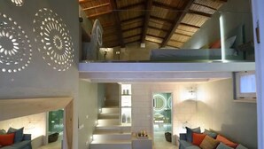 Ein geräumiger Wohnbereich mit Treppe zu einem Balkon, einer Sofagarnitur und einem modernen Badezimmer mit Waschtisch und Spiegel.