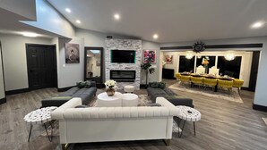 Ein modernes Wohnzimmer mit einem weißen Sofa, einem Kamin, einem Essbereich mit gelben Stühlen und einem an der Wand befestigten Fernseher.