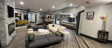 A modern living room with a stone fireplace, a grey sectional sofa, and a dining area with yellow chairs.