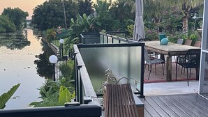 Eine Holzterrasse mit Tisch und Stühlen mit Blick auf ruhiges Wasser und üppiges Grün.