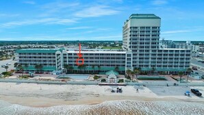 Un hôtel à plusieurs étages doté d’un toit végétalisé, situé près d’une plage au rivage sablonneux et bordé d’un petit plan d’eau.