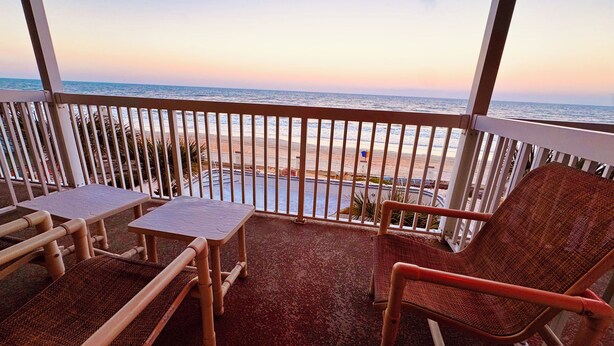 Un balcon avec deux fauteuils en osier et une petite table, donnant sur une plage et l’océan.