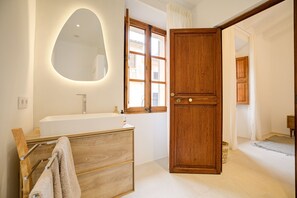 Une salle de bain avec un meuble-lavabo en bois, un lavabo blanc, un miroir et une porte en bois.