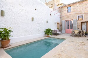 Une piscine avec un mur blanc et une terrasse en pierre.