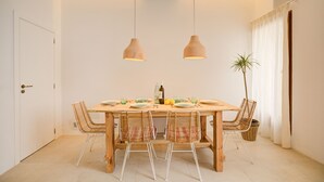 A dining area with a wooden table, four wicker chairs, two pendant lights, and a potted plant.