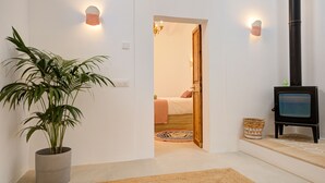 A room with a potted plant, a wooden door leading to another room, a small black stove, and a woven basket on the floor.