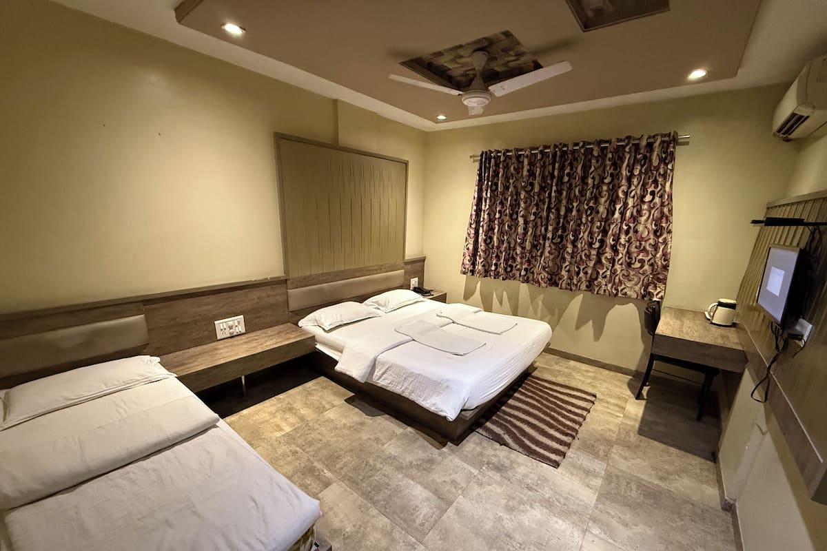 Ein Hotelzimmer mit einem großen Bett, zwei kleineren Betten, einem Schreibtisch mit Stuhl, einem Fernseher und einem Deckenventilator.