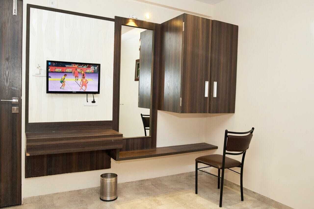 Ein Zimmer mit an der Wand montiertem Fernseher, einem Holzschrank, einem Stuhl und einem Mülleimer.