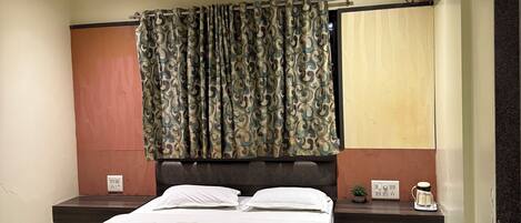 A bedroom with a bed, nightstands, a ceiling fan, a window with curtains, and a wall-mounted air conditioner.