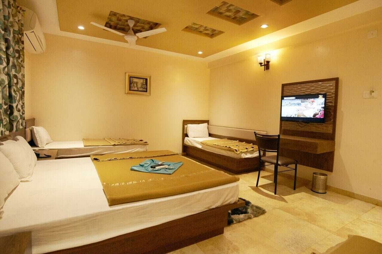 A hotel room with two beds, a desk, a television, and a ceiling fan.