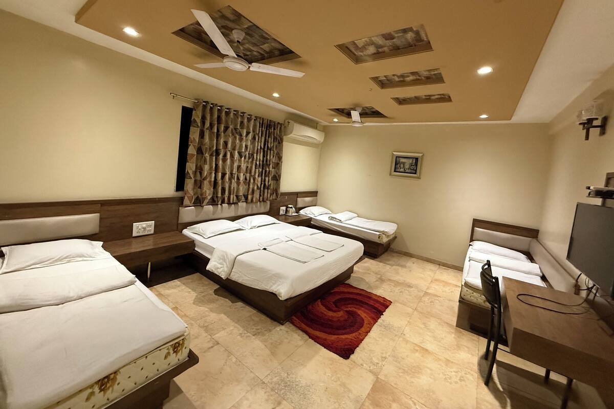 Ein Hotelzimmer mit zwei Betten, einem Schreibtisch, einem Stuhl, einem Deckenventilator und einem roten Teppich.