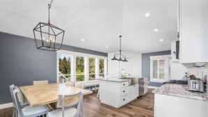 A modern kitchen with white cabinets, a wooden dining table, and a large island.