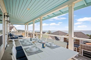 A covered outdoor dining area with a table set for four, overlooking a residential neighborhood and the ocean.