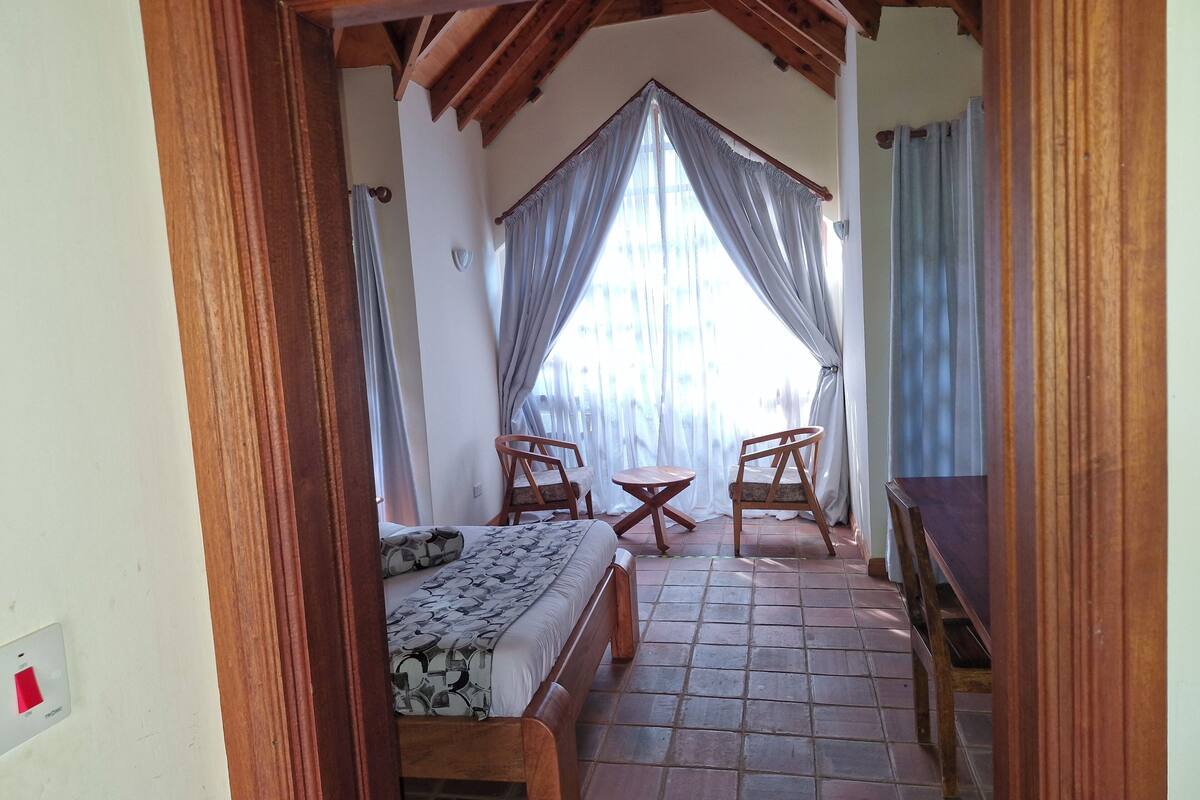 A bedroom with a bed, two chairs, a small table, and a window with curtains.