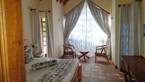 A bedroom with a bed, two chairs, a small table, and a wooden desk. - OD KIDI COTTAGES  (Migori)