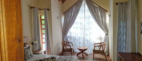 A bedroom with a bed, two chairs, a small table, and a wooden desk.