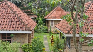 A row of stone cottages with red-tiled roofs, surrounded by lush greenery and a stone pathway. - OD KIDI COTTAGES  (Migori)