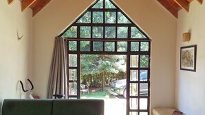 A cozy room with a green sofa, a wooden coffee table, and a bench. A large window with a view of the outdoors is visible. - OD KIDI COTTAGES  (Migori)