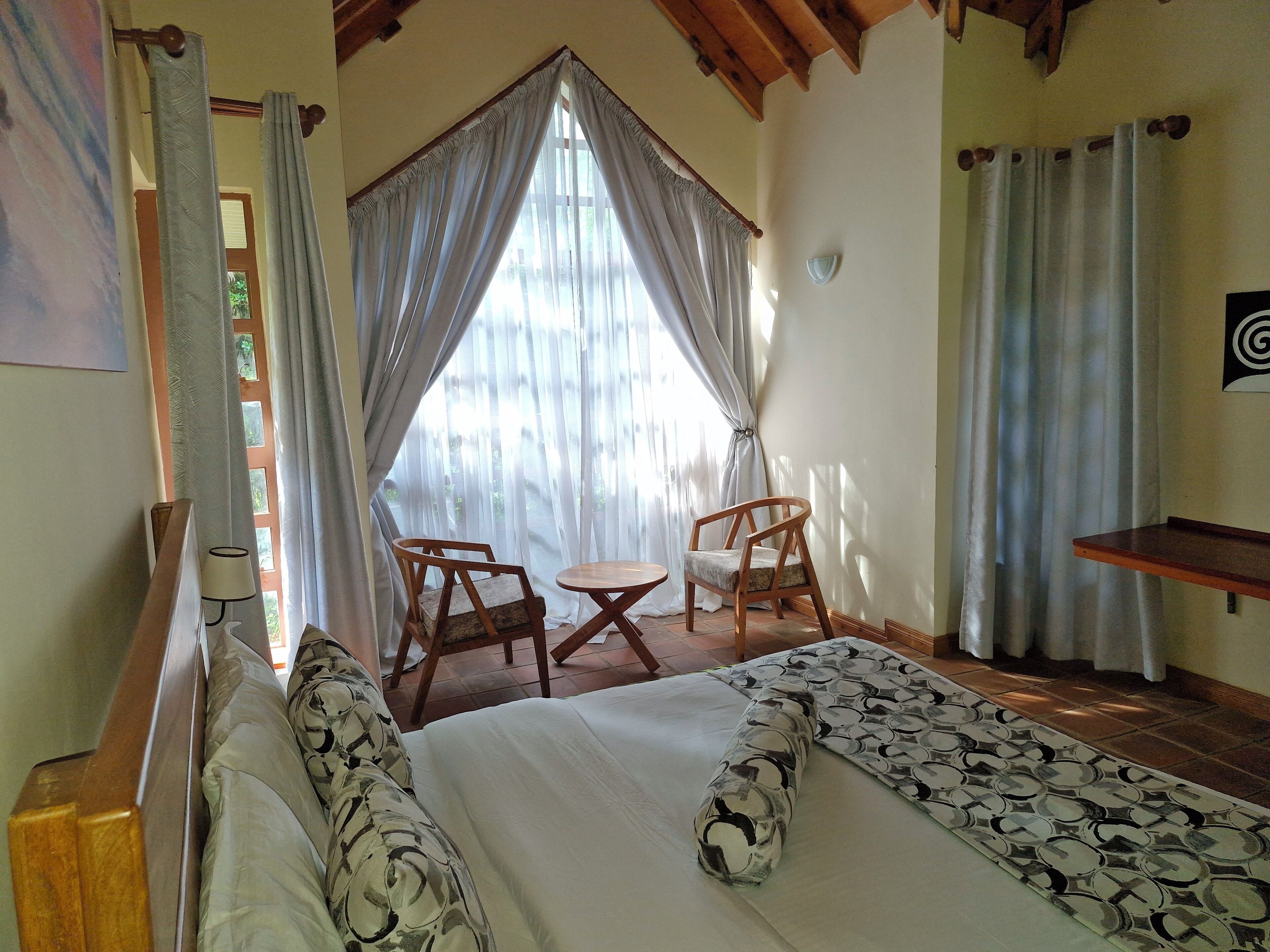 Ein Schlafzimmer mit einem Bett, zwei Holzstühlen, einem kleinen Tisch und einem Regal.