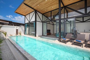 A modern pool area with clear blue water, lounge chairs, and a wooden ceiling structure. - 17m Oxygen Pool Villa Sunset Garden 11 (Rawai)