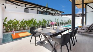 A modern outdoor dining area with a pool, surrounded by plants and a clear blue sky. - 17m Oxygen Pool Villa Sunset Garden 11 (Rawai)