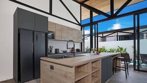 A modern kitchen with a wooden island, black appliances, and a large window overlooking a balcony. - 17m Oxygen Pool Villa Sunset Garden 11 (Rawai)