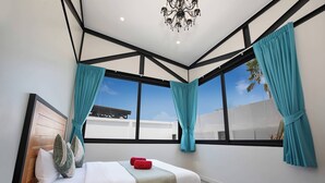 A modern bedroom with a bed, teal curtains, a chandelier, and large windows. - 17m Oxygen Pool Villa Sunset Garden 11 (Rawai)