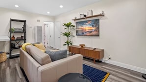Een moderne woonkamer met een beige bank, een houten console tafel en een groot schilderij van een zonsondergang.