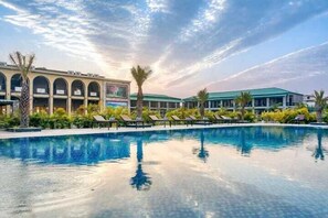 A swimming pool with lounge chairs and a building with arched windows. - Corbett Elegant Retreat (Ramnagar)