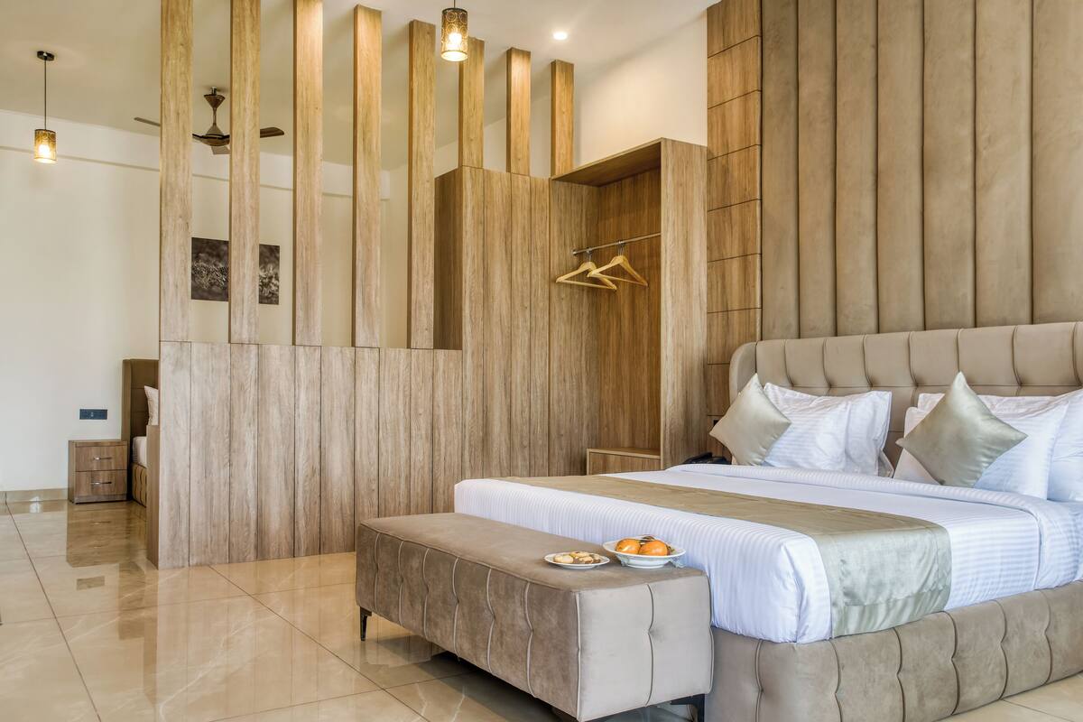 A modern bedroom with a large bed, a bench, a wardrobe, and a hanging light fixture.