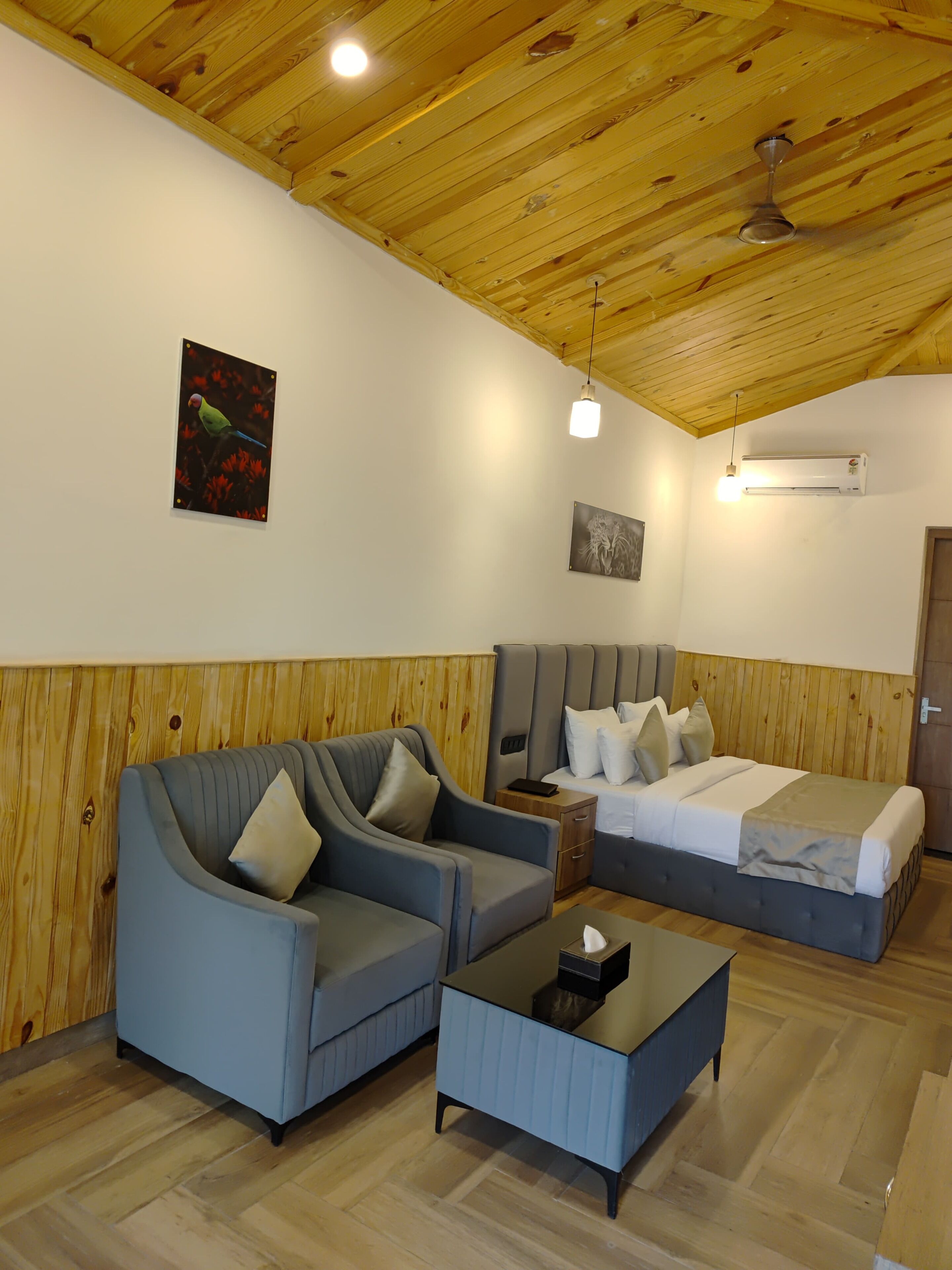 A room with a wooden ceiling, a bed, a sofa, a small table, and a wall-mounted air conditioner.