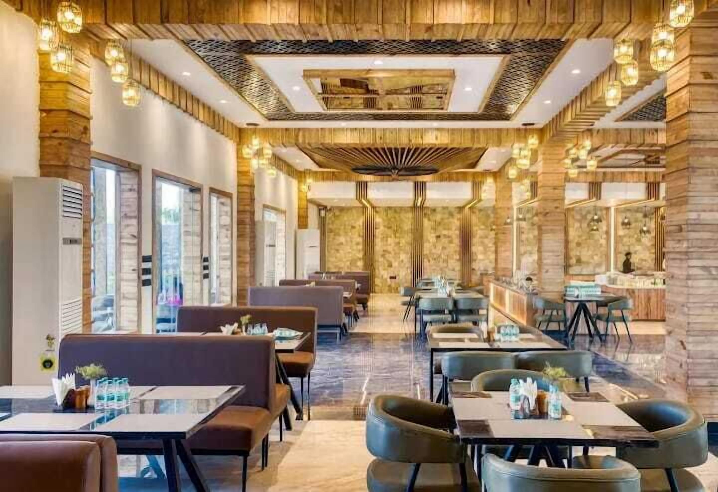 A modern restaurant with wooden paneling, pendant lighting, and a central bar area.