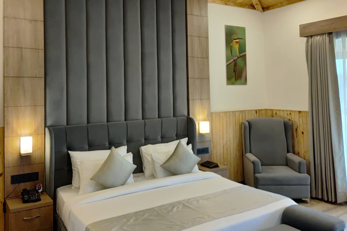 A bedroom with a large bed, a grey upholstered headboard, bedside tables with lamps, a grey armchair, and a wooden ceiling.
