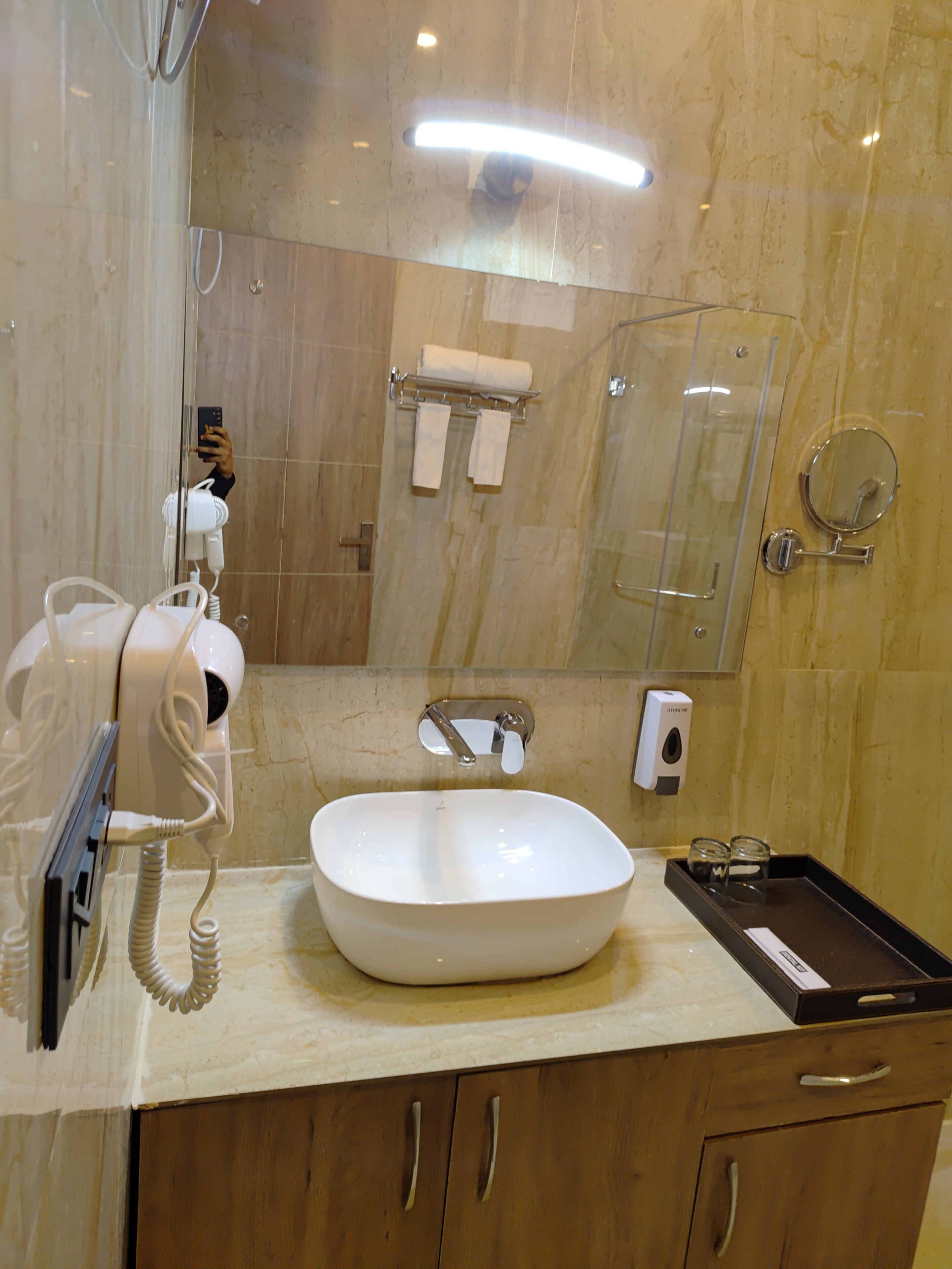 Ein Badezimmer mit weißem Waschbecken, Fön, Handtuchhalter, Spiegel und Seifenspender.