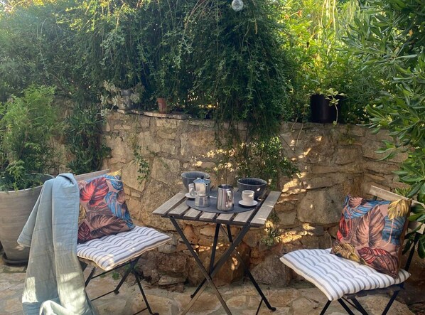An outdoor patio with a stone wall, two cushioned chairs, a small table with a coffee pot, cups, and a bowl. - La Dolce Nikka (Rovinj)
