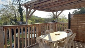 A wooden deck with a table and chairs, overlooking a garden and trees.