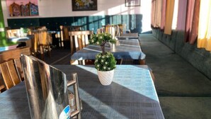 A restaurant with long tables, a potted plant, and a metal chair. - Crane Valley Cottage (Leh)