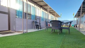 A building with a covered outdoor seating area and artificial grass. - Crane Valley Cottage (Leh)