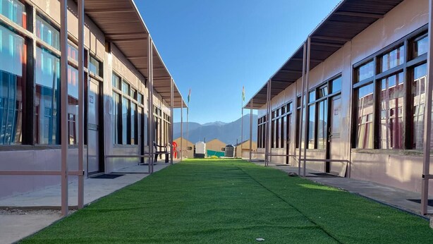 A building with a central green lawn, large windows, and a clear sky. - Crane Valley Cottage (Leh)