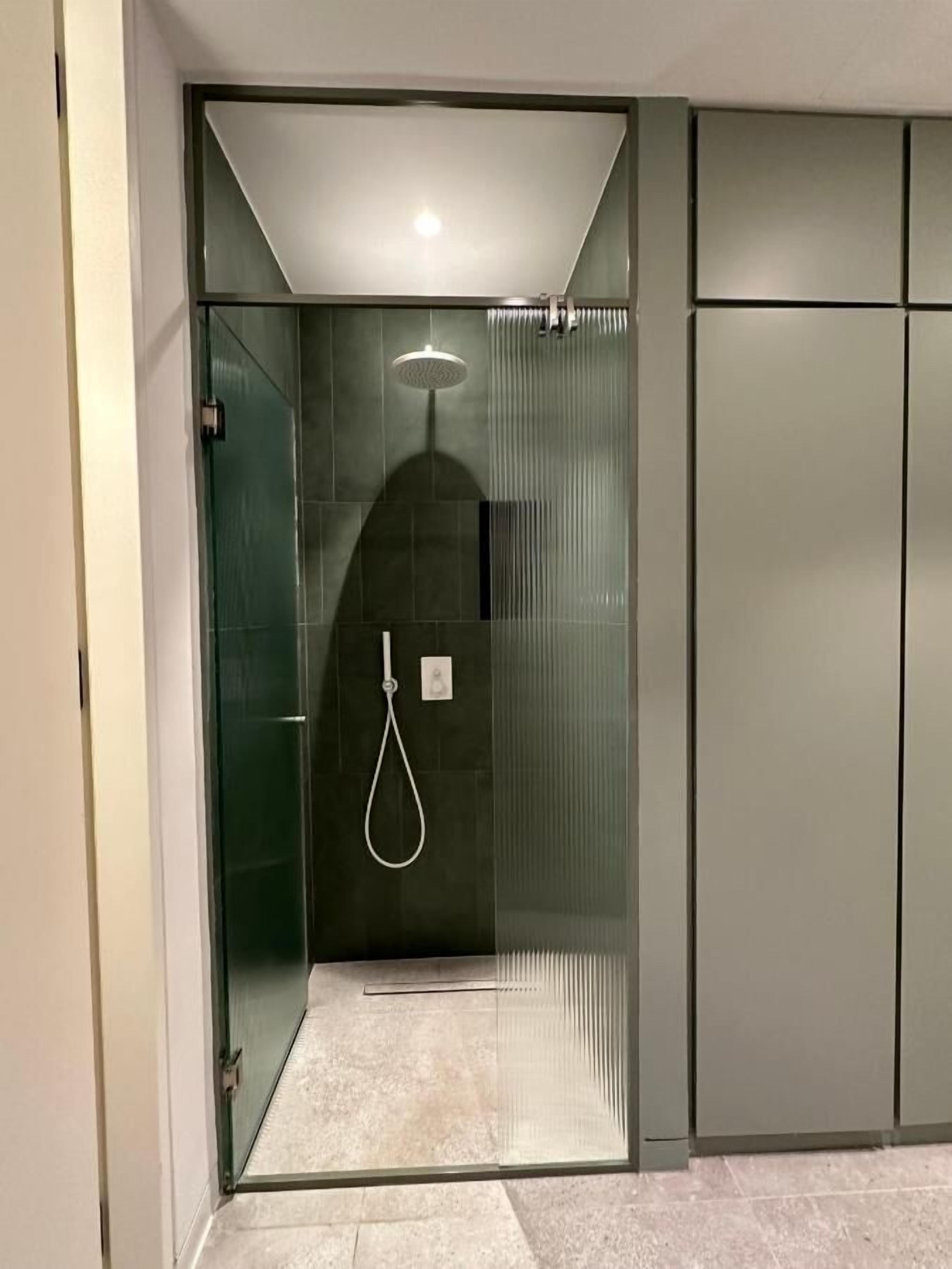 Eine moderne Duschkabine mit Glastür, Handbrause und fest installierter Armatur.