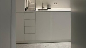A modern kitchen with white cabinets, a stainless steel sink, and a built-in range hood. - Suite No1 (Rethymno)
